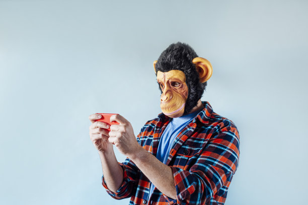 戴着猴子面具的男子使用智能手机。图片下载