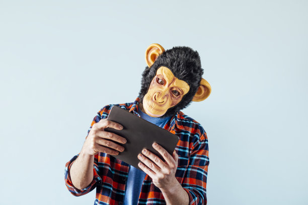 戴着猴子面具的人正在使用平板电脑。图片下载