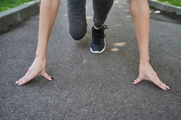 女运动员在室外跑步起跑位置。准备好了!女运动员站在体育场跑道的起跑线上，准备跑步。健身女孩正准备从低起点跑步。图片下载