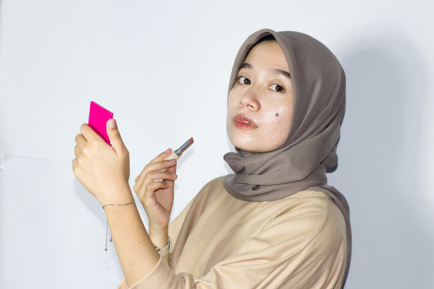 年轻的戴头巾的妇女拿着口红或润唇膏。孤立的白色背景图片下载