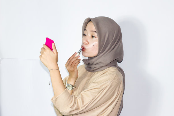 年轻的戴头巾的妇女拿着口红或润唇膏。孤立的白色背景图片下载