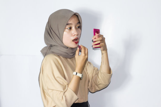 年轻的戴头巾的妇女拿着口红或润唇膏。孤立的白色背景图片下载