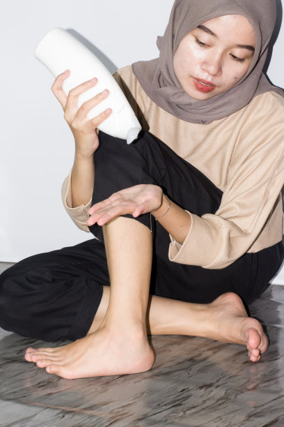 戴头巾的年轻女性涂抹腿霜、乳液或保湿霜的女性。皮肤护理。美女脚上涂着奶油图片下载