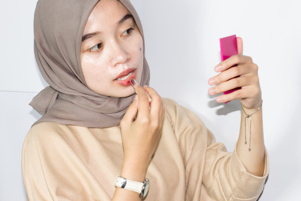年轻的戴头巾的妇女拿着口红或润唇膏。孤立的白色背景图片下载