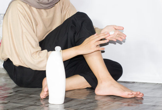 戴头巾的年轻女性涂抹腿霜、乳液或保湿霜的女性。皮肤护理。美女脚上涂着奶油图片下载