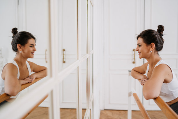 漂亮的西班牙女孩站在镜子微笑靠在芭蕾舞吧台在舞蹈课上微笑满意的成就。年轻漂亮的女人很高兴能保持健康。
健身，有目标的人。图片下载
