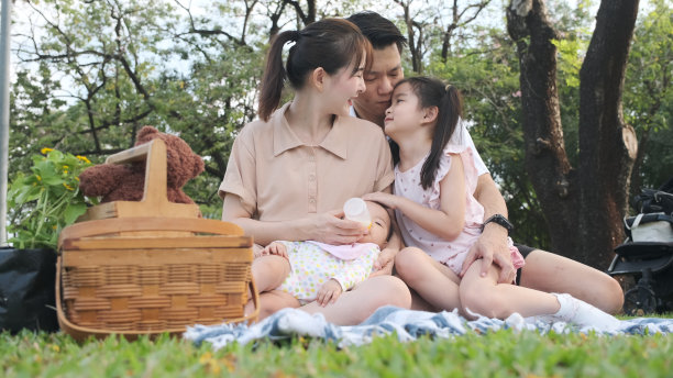 年轻的亚洲母亲用奶瓶喂她的女儿和她的家人在公园野餐。图片下载