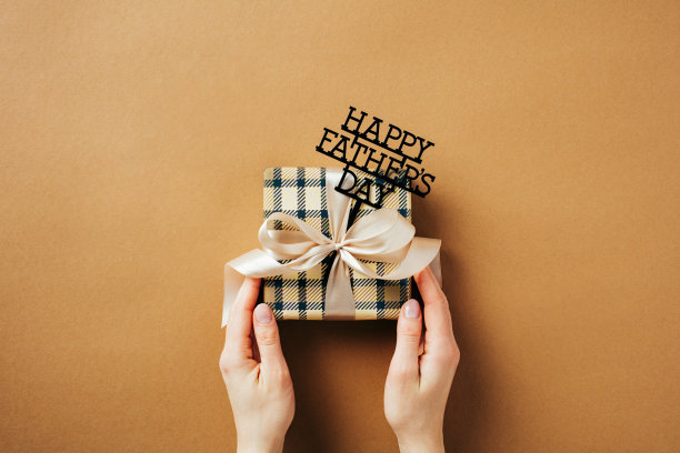 父亲节快乐的概念。女性手拿着标有“父亲节快乐”字样的老式礼品盒，背景为棕色。图片下载