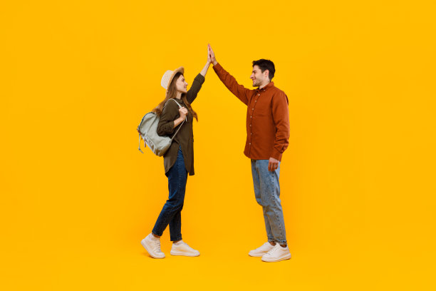 快乐的游客夫妇站在黄色背景下击掌图片下载