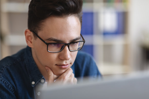 年轻英俊的男子在眼镜看着电脑屏幕的肖像图片下载