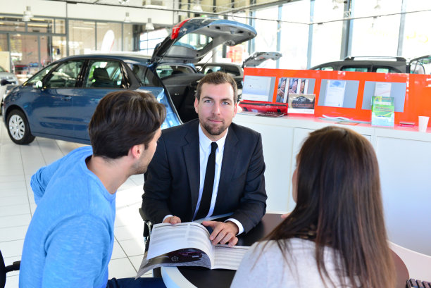 一对年轻夫妇在一家汽车经销店的陈列室里购买一辆新车，与卖方签订销售合同图片下载
