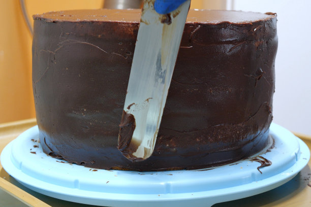 糕点师正在用抹刀在蛋糕两侧涂抹奶油，特写。烹饪，烘焙和烹饪的食物概念，家庭烹饪图片下载