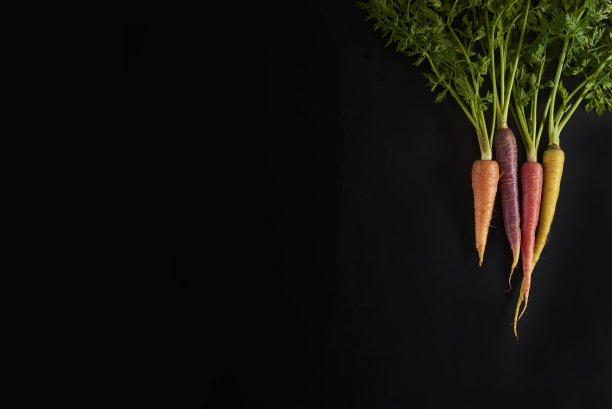 在有机蔬菜水果店用叶子给胡萝卜上色。股票的照片。图片下载