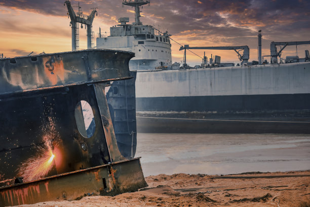 一艘大型油轮在港口拆船，工人通过焊接切割零件，背景是巴基斯坦加达尼拆船场的沉船和日落图片下载