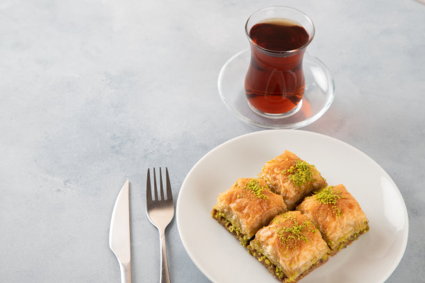 传统的开心果果仁蜜饼配土耳其茶。浅蓝色背景上的果仁蜜饼图片下载