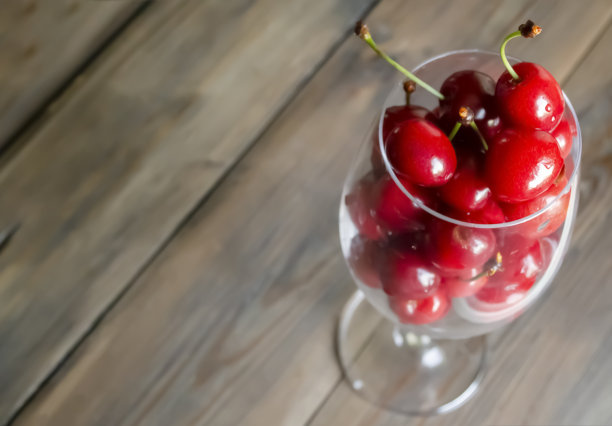 杯子里的樱桃。在木制背景上是一个有浆果的玻璃杯。杯子里是红色的樱桃浆果。夏天的浆果是一种健康食品。新鲜的樱桃汁。图片下载