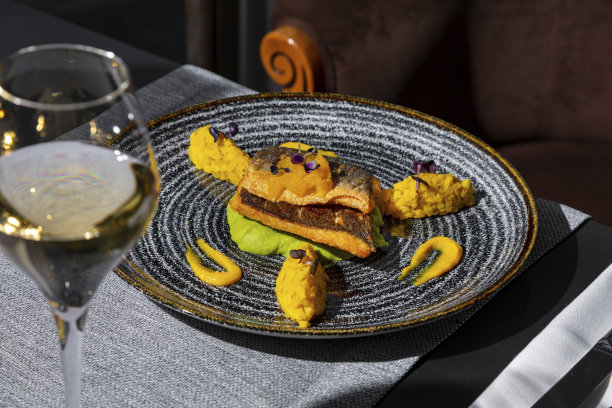 炸鱼配土豆泥、豆芽、芒果和酱汁，放在桌子上的盘子里，配上餐巾、餐具和一杯酒图片下载