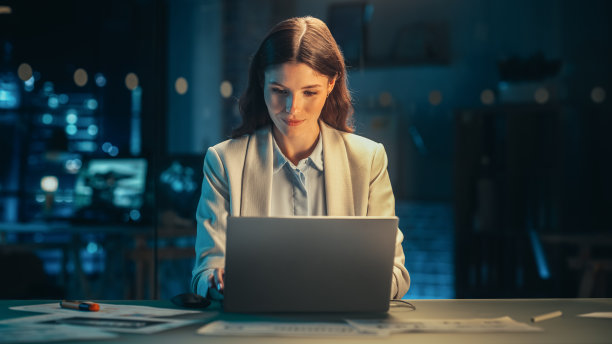 戴眼镜的时尚女性晚上在公司办公室用笔记本电脑工作。年轻的经理浏览互联网，网上购物，阅读朋友和同事的社交媒体帖子。图片下载