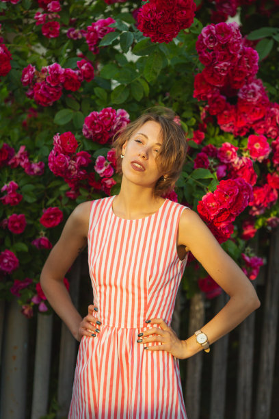 金发女人在背景上的玫瑰灌木。花园。春天的背景图片下载