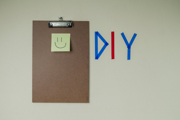 用彩色胶带在墙上DIY写字，旁边有一个剪贴板和一个笑脸笔记贴纸。图片下载