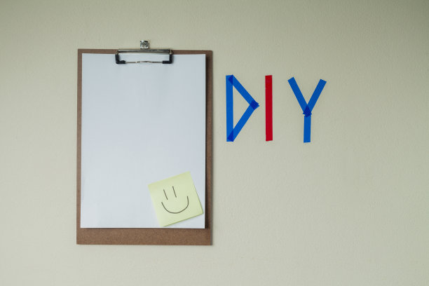 用彩色胶带在墙上DIY写字，旁边有一个剪贴板和一个笑脸笔记贴纸。图片下载