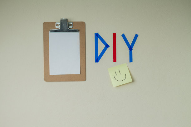 用彩色胶带在墙上DIY写字，旁边有一个剪贴板和一个笑脸笔记贴纸。图片下载