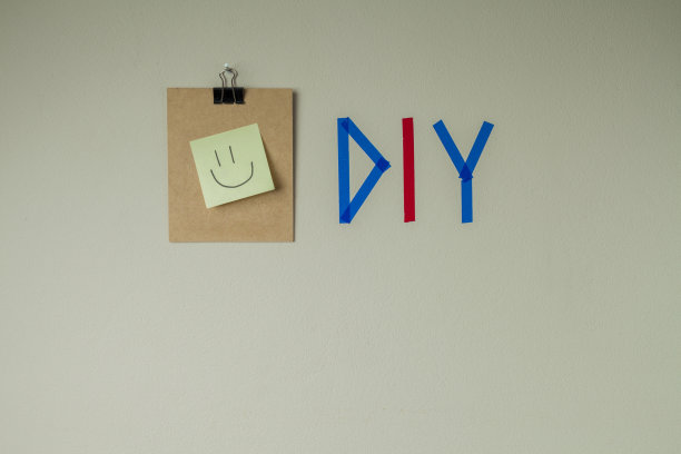 用彩色胶带在墙上DIY写字，旁边有一个剪贴板和一个笑脸笔记贴纸。图片下载