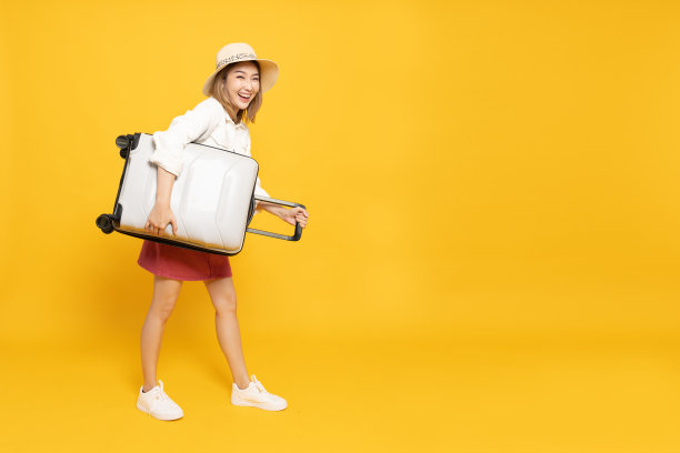 快乐的亚洲女子旅行者站着，拿着行李箱孤立在黄色背景，旅游女孩有快乐的假期旅行概念，全身构图图片下载