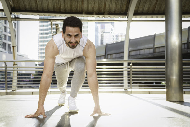 亚洲运动跑男在商务工作结束后沿着城市进行户外跑步运动前伸展和热身腿部肌肉。户外健身。图片下载
