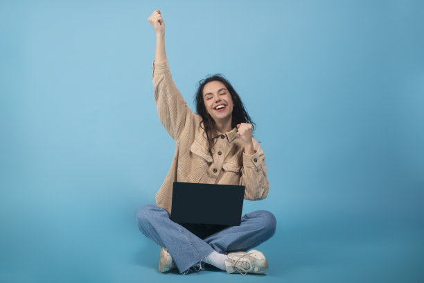 欢喜兴奋的千禧欧洲女学生坐在地板上笔记本电脑，庆祝胜利和成功图片下载