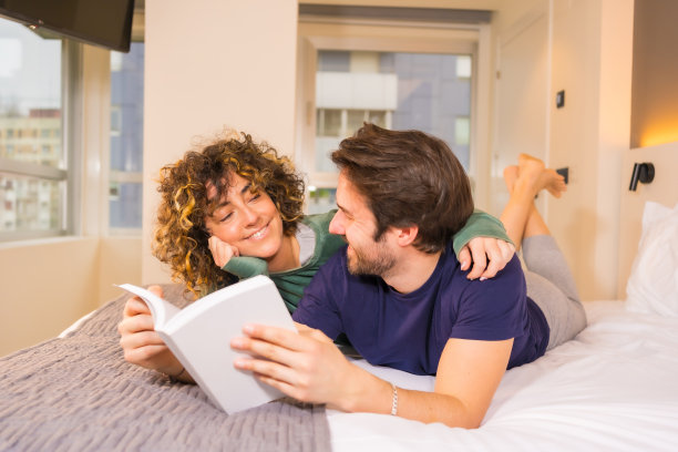 一对可爱的夫妇躺在床上读一本有趣的书的特写镜头图片下载