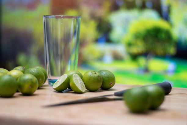 一张摆着许多柠檬、一把刀和一个空杯子的桌子，背景是后院的散景图片下载