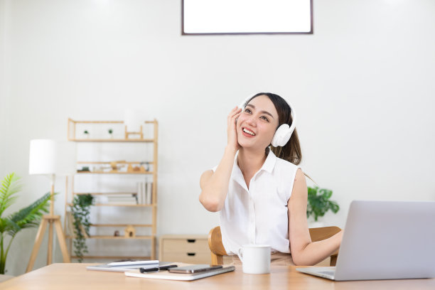 漂亮的亚洲女孩戴着耳机在笔记本电脑和手机上开心地听音乐。享受假期在工作时听音乐，在家办公的概念。图片下载