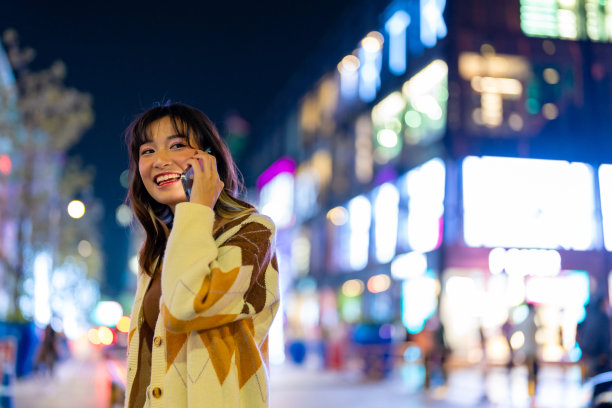 年轻的亚洲女人晚上在城市里打电话。图片下载