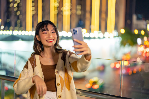 年轻的亚洲女子晚上在城市里用手机自拍。图片下载