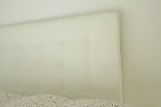 柔软的床头板。真皮或人造皮革和织物制成的家具内饰。柔软的床头板靠在轻墙上。图片下载