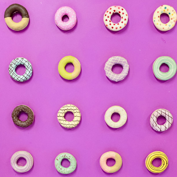 圆形甜甜圈食物与不同的装饰在坚实的紫粉色背景图片下载