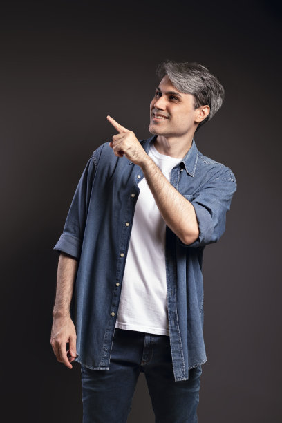 一个巴西男人的肖像，穿着纽扣衬衫和牛仔裤，微笑着指着一边，灰色的头发-彩色照片-巴西图片下载