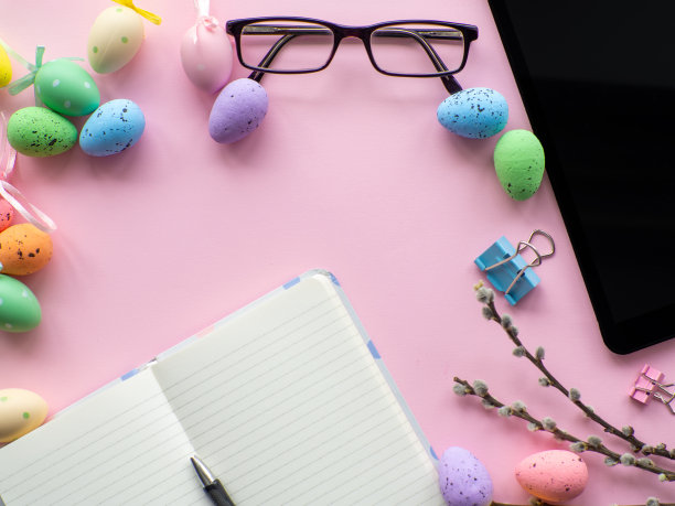 工作桌上的设备和复活节彩色鸡蛋在粉红色的背景图片下载