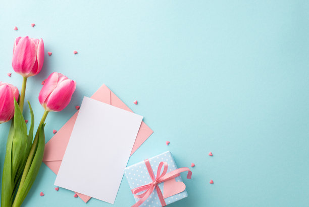 母亲节庆祝概念。顶部视图照片的捧粉郁金香小蓝色礼盒与蝴蝶结信封纸单和洒在孤立的粉彩蓝色背景与复制空间图片下载