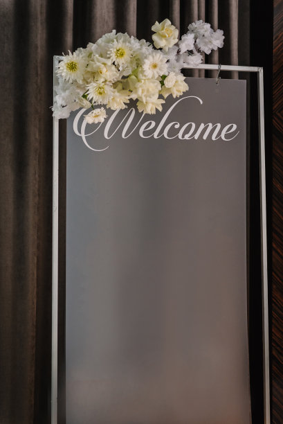 婚礼入口处为客人准备的标志——“欢迎光临”。带文字位置的板子:餐厅客人在餐桌上的座位区域。婚宴。框架上装饰着鲜花。文本空格。特写镜头。图片下载