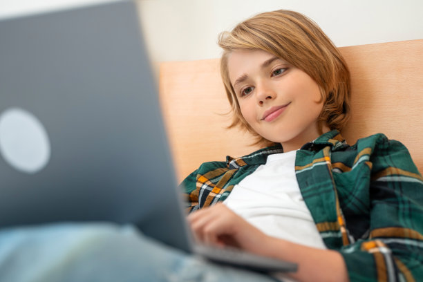 聪明的白人中学男孩使用笔记本电脑。孩子在键盘上打字。玩电子游戏。在线导师数字课堂，在家电脑上进行网络教学。虚拟教育。电子教育。图片下载