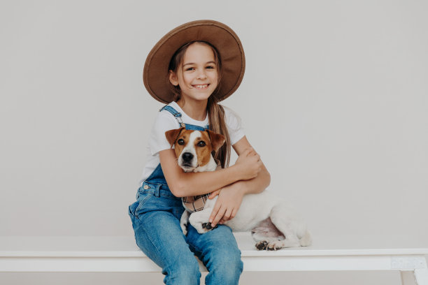 室内拍摄可爱的小女孩穿着时尚的衣服，抱着杰克罗素梗狗，和最好的动物朋友玩耍，彼此相爱。孩子，宠物和友谊的概念图片下载