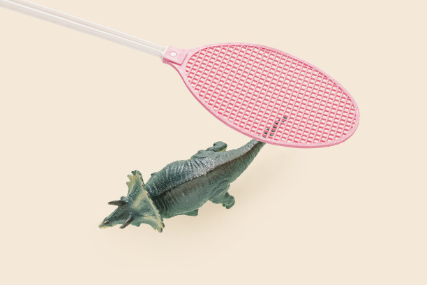 米色背景上粉红色苍蝇拍和恐龙的侵略或战争失败方的抽象概念。均势或以弱攻强。恐龙如何灭绝的有趣想法。图片下载