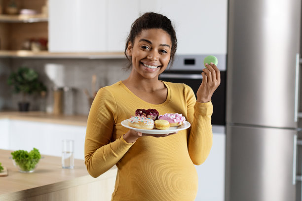 快乐快乐的年轻黑人孕妇大肚子吃糖果，享受一盘饼干图片下载