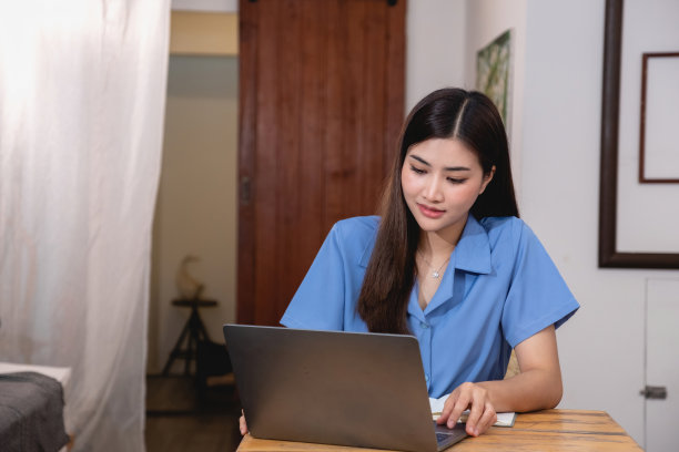 一个有着美丽笑容和面容的亚洲女人舒适地坐在家里的桌子上，带着笔记本电脑和笔记本电脑，在一个明媚的早晨放松和放松。假期假期概念。图片下载