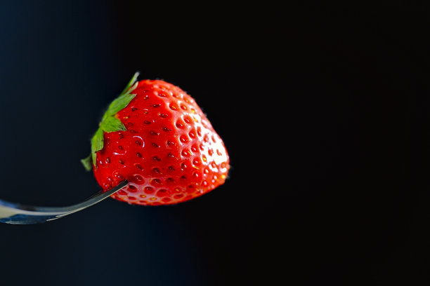 新鲜草莓粘在叉子上，黑色背景图片下载