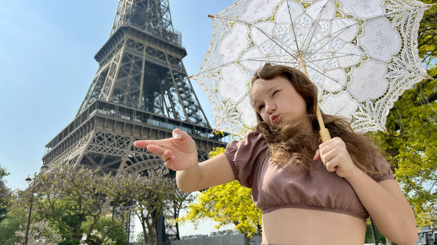 一个美丽的年轻女孩穿着夏天的连衣裙站在埃菲尔铁塔的背景下，带着蕾丝伞，她举起她的手，好像有一个广告旅行社起飞的地方图片下载