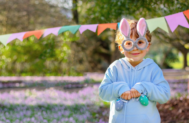 小男孩戴着花哨的眼镜，戴着兔子耳朵在花园里。复活节兔子滑稽服装。庆祝、聚会、装饰图片下载