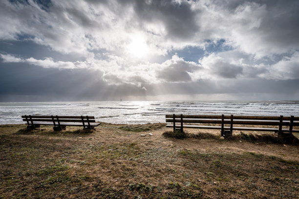 法国雷岛里韦杜海滩上的木制长凳。太阳在乌云中闪耀。图片下载